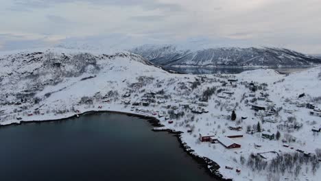 vista del avión no tripulado en el área de tromso en invierno volando sobre un fiordo hacia una pequeña ciudad nevada con pequeñas casas en noruega