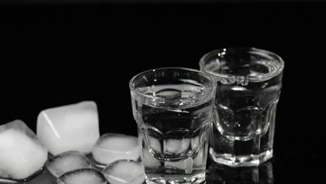 pour vodka into shot glasses with ice cubes placed on a black background