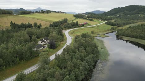 upwards movement from the calm reflective lake in norway over the road towards the green grass covered mountains with view over red and yellow traditional houses