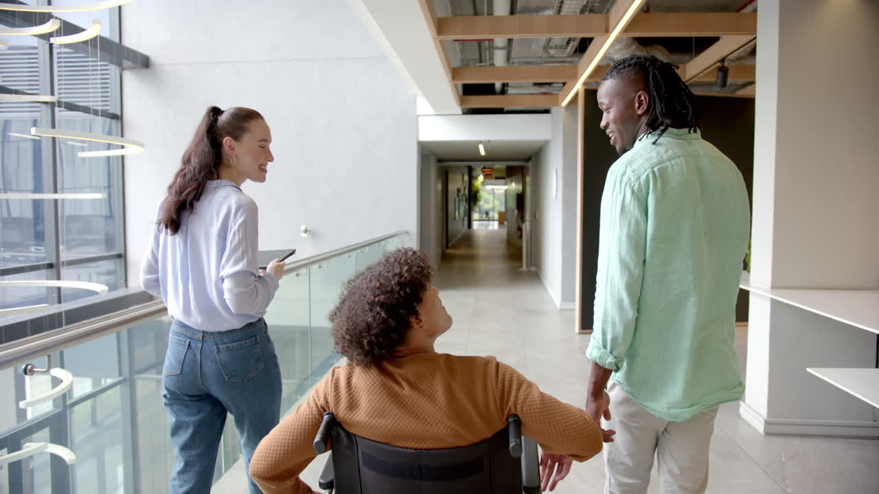 Colleagues in office hallway, man in wheelchair discussing with coworkers