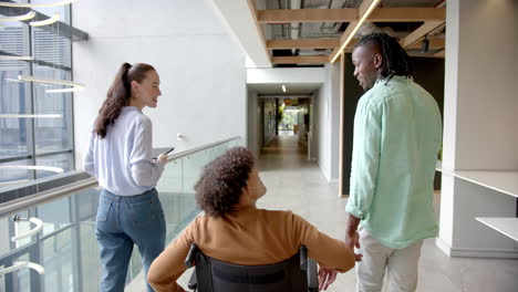 colleagues in office hallway, man in wheelchair discussing with coworkers