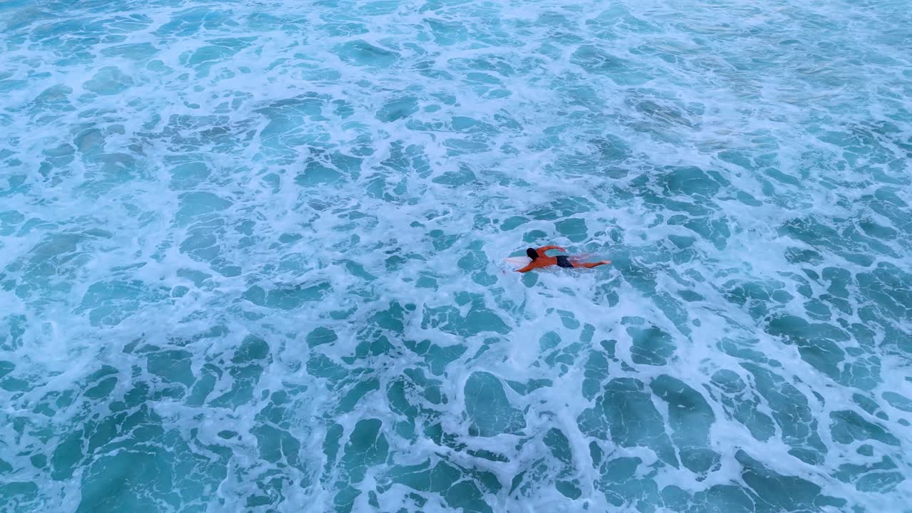 Drone aerial footage of a lone surfer paddling out on his surfboard during a golden sunset in Weligama, Sri Lanka.