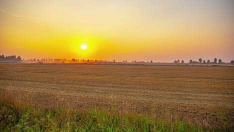 Cinematic-timelapse-of-tractors-working-on-a-field-while-the-sun-is-setting-in-the-background-on-a-beautiful-and-cloudless-day