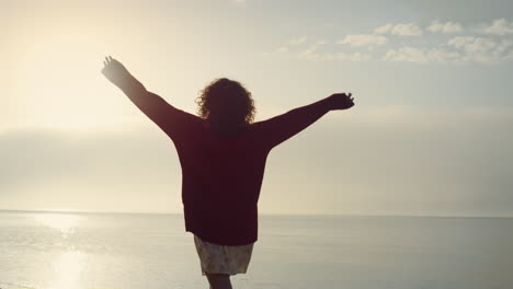 Casual-girl-walking-on-seashore-at-sunrise.-Positive-woman-raising-hand