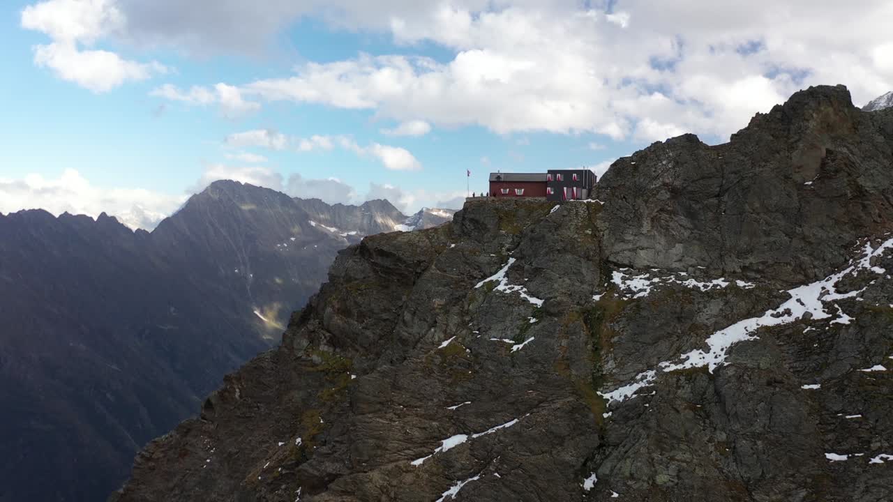 toma aérea sobrevolando la cabaña dossen con la bandera suiza junto al acantilado empinado que baja al valle de los alpes en la región montañosa