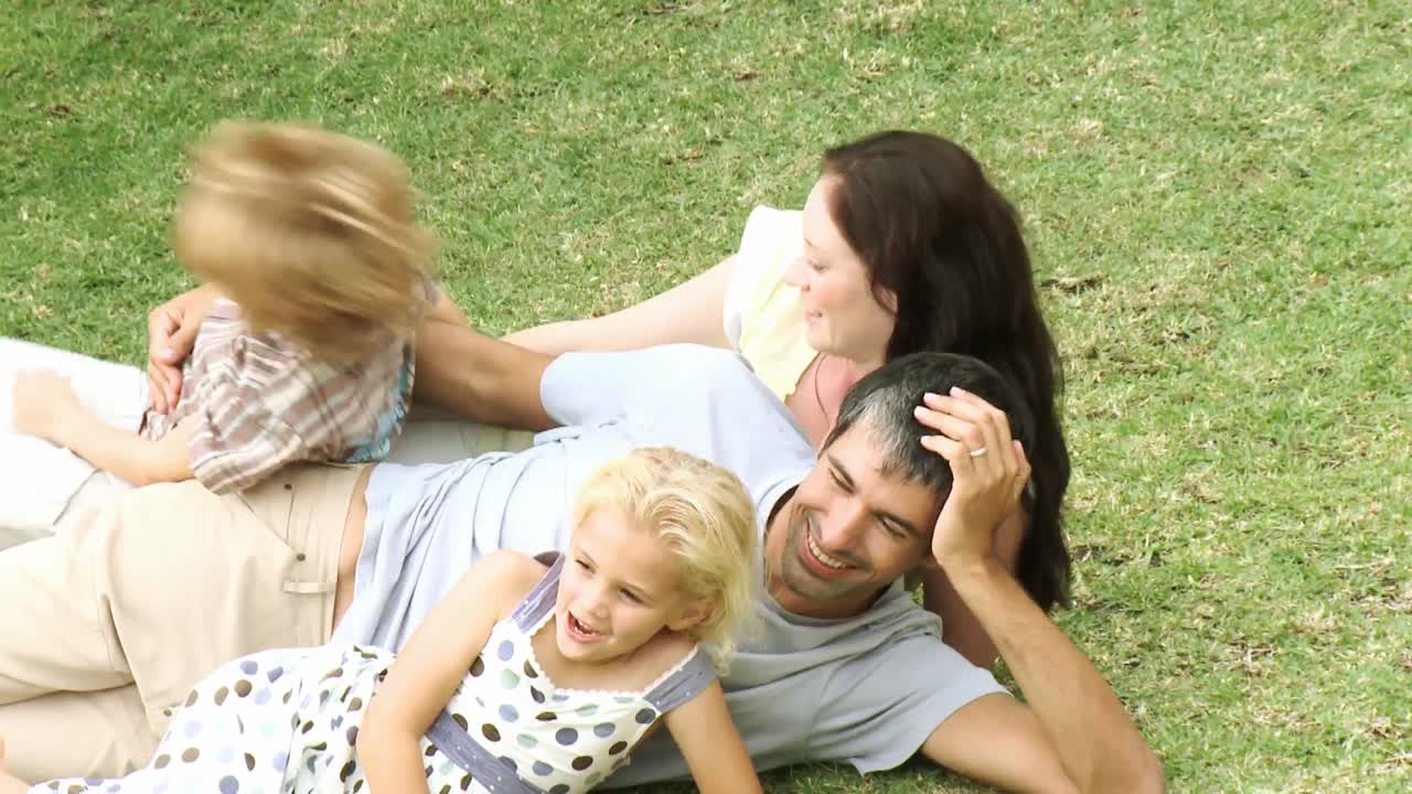 Famiglia felice sull'erba che saluta la telecamera