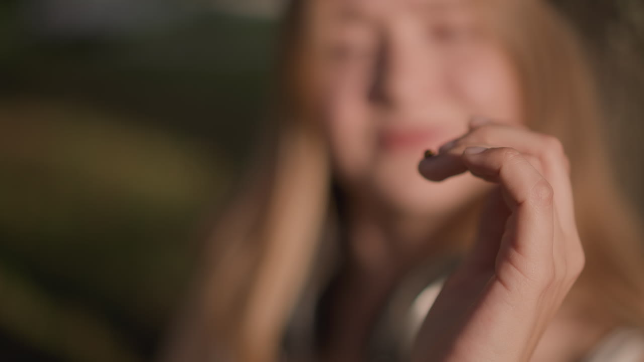 Giovane donna all'aperto con cuffie e coccinella sulla punta del dito, sequenza giocosa e illuminata dal sole che mostra una ballerina che si gode la musica, gesti espressivi delle mani, tonalità della pelle morbide e bokeh caldo, scena candida in un parco
