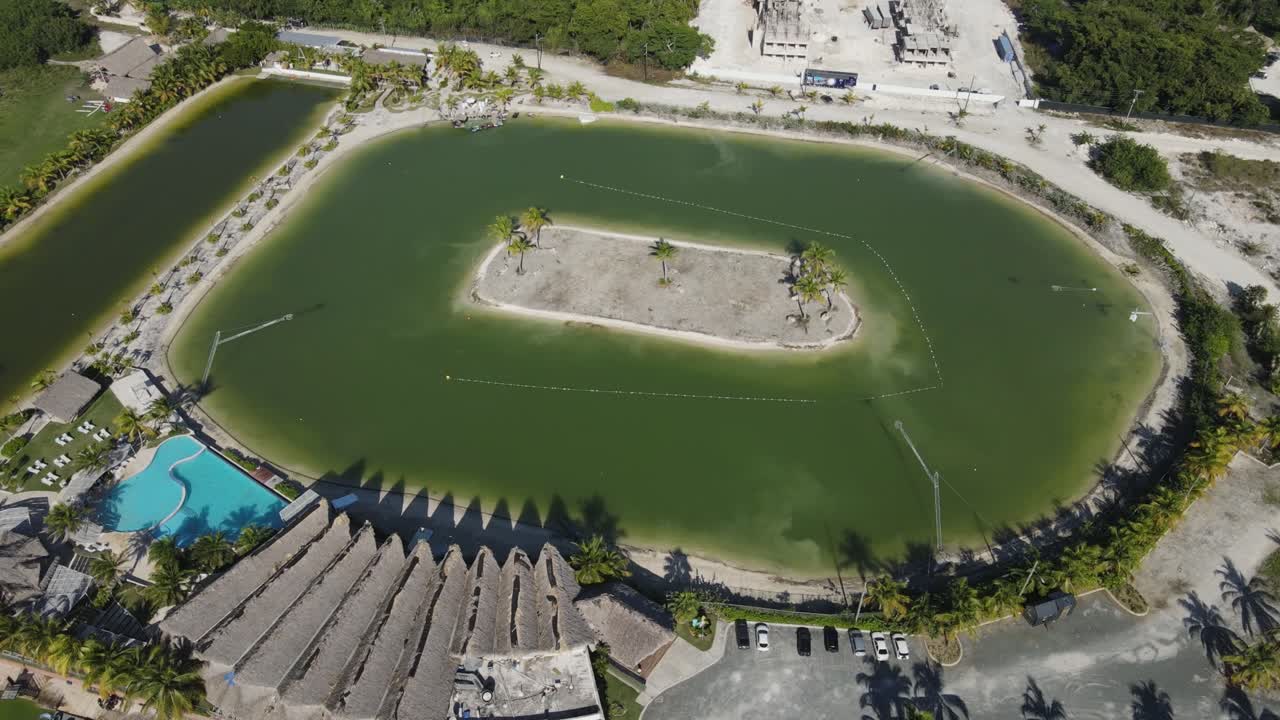 Orbit wide shot of Caribbean lake park in Punta Cana, Dominican Republic. Sunny tropical day with palm trees and sandy islands. The water is dark green.