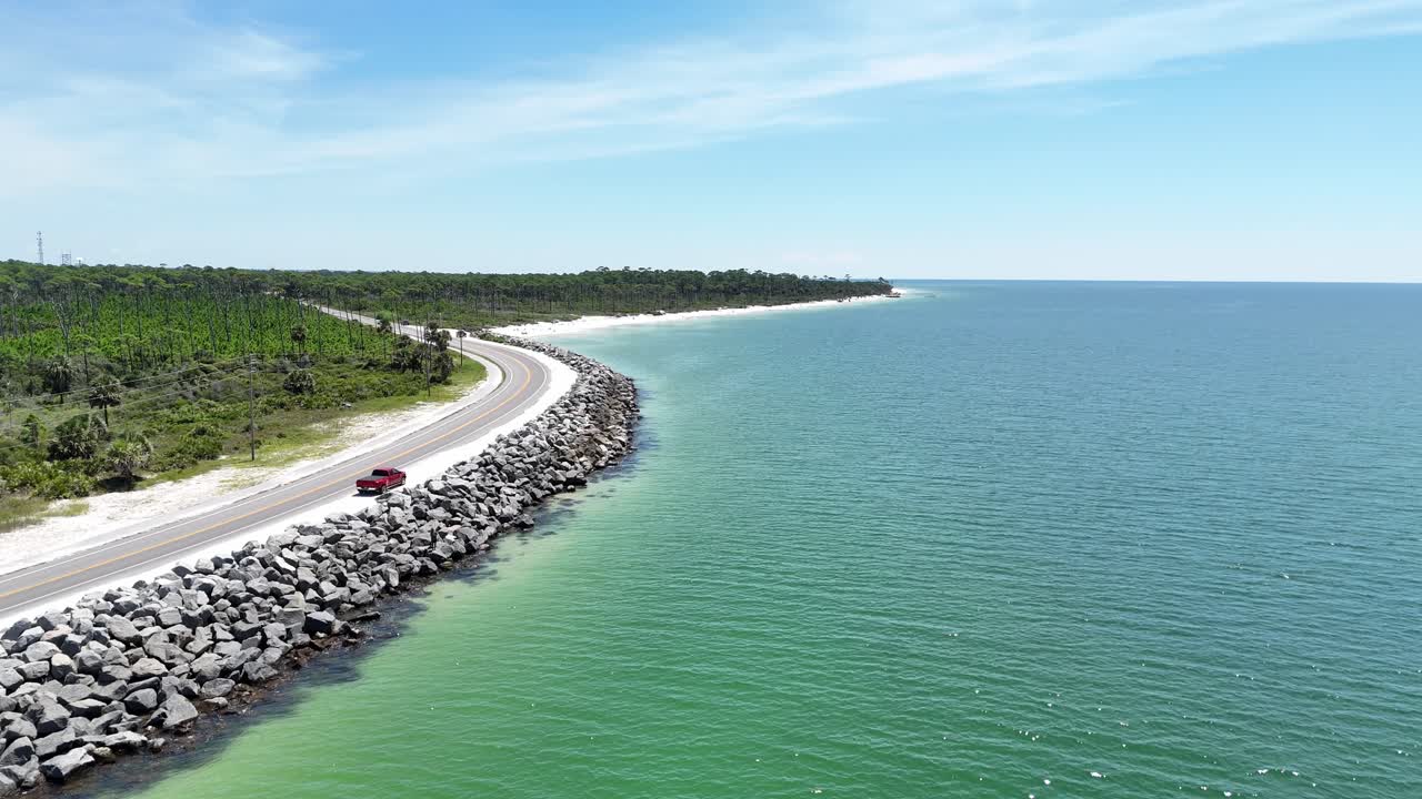 Dinamica ripresa aerea di un drone sul frangiflutti in pietra che costeggia la strada litoranea vicino all'acqua di mare turchese, Cape San Blas, Gulf County, Florida, USA