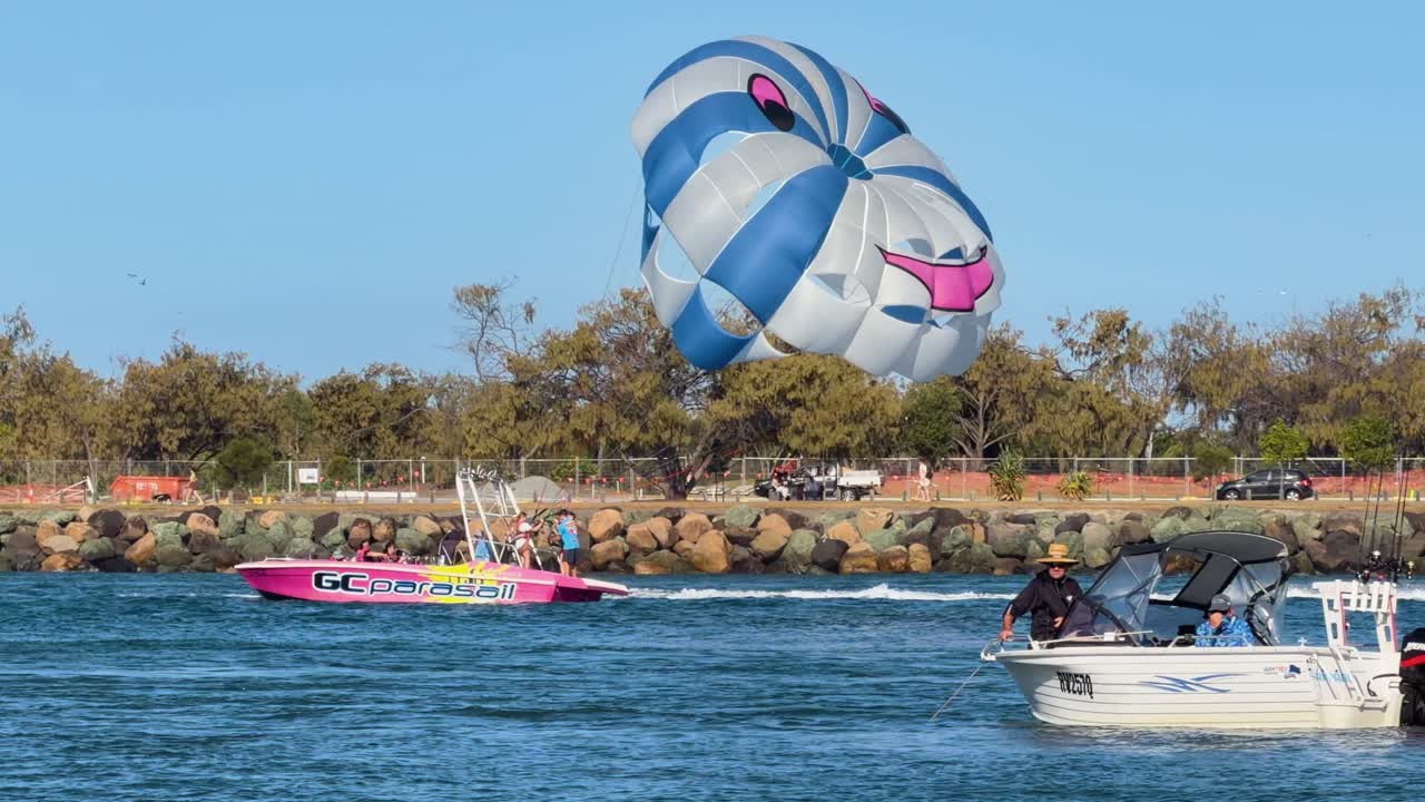 Parasailing boat tows colorful parachute across sunny Gold Coast waterway, clear skies, steady camera