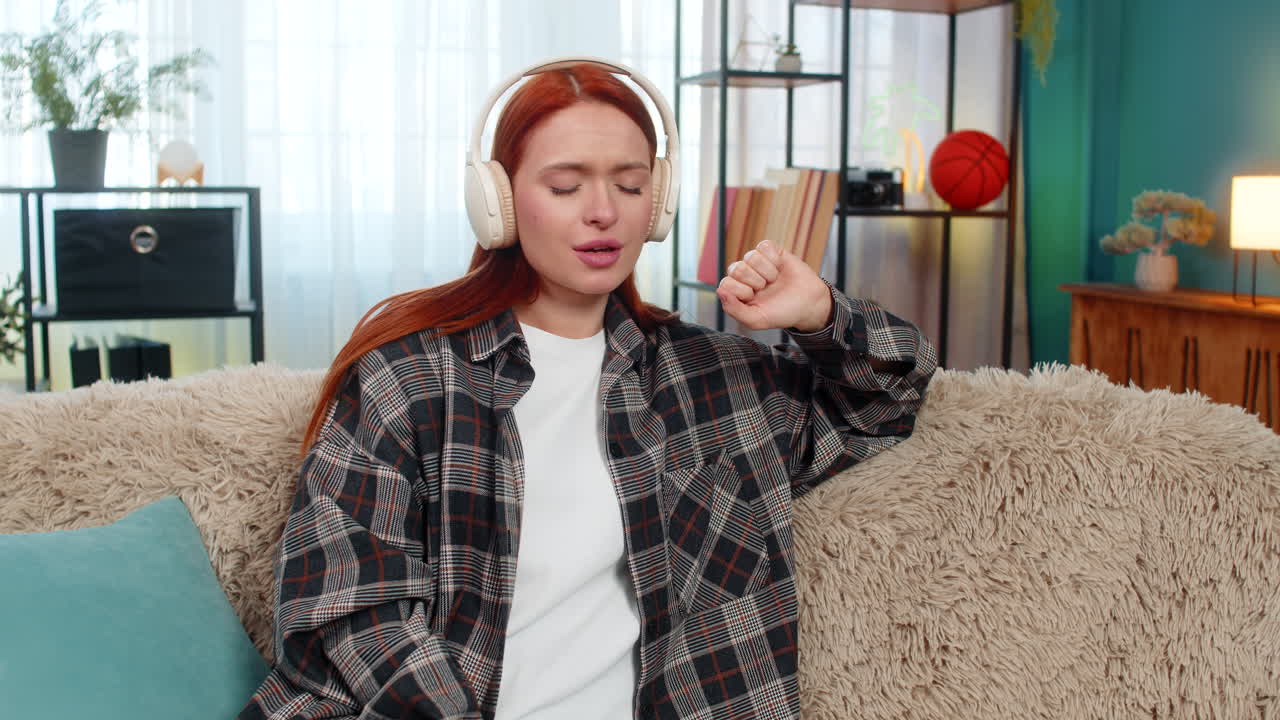 Woman sitting on sofa wearing wireless headphones listening to music with closed eyes relaxing calm