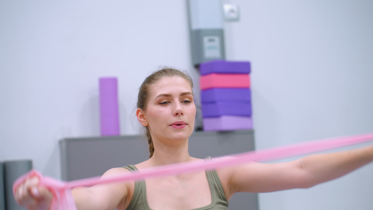 Focused woman works out by stretching a resistance band with arms raised in a brightly lit gym, demonstrating strength and flexibility training