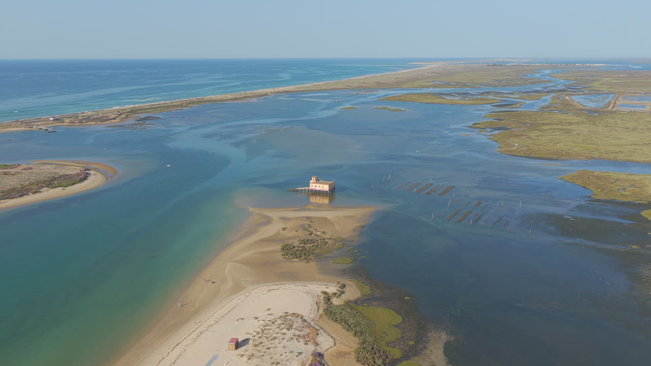 Descending aerial view of Fuzeta lagoon with rescue station and winding sandbank