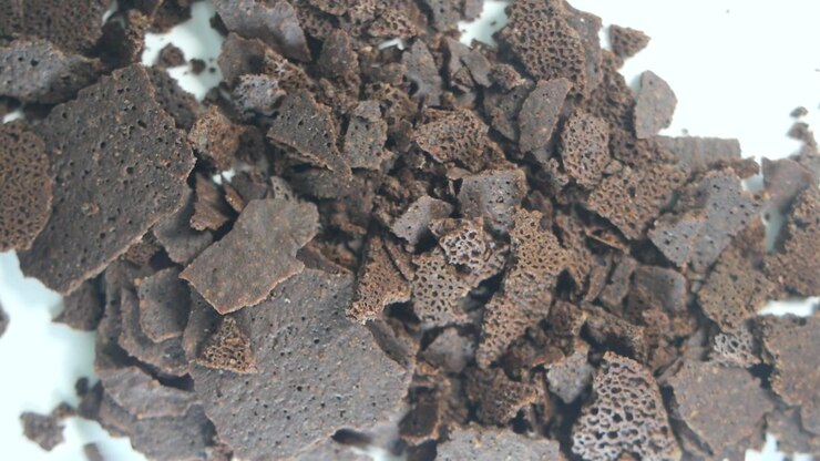 Scaglie di cioccolato fondente che cadono su un mucchio su sfondo bianco.
