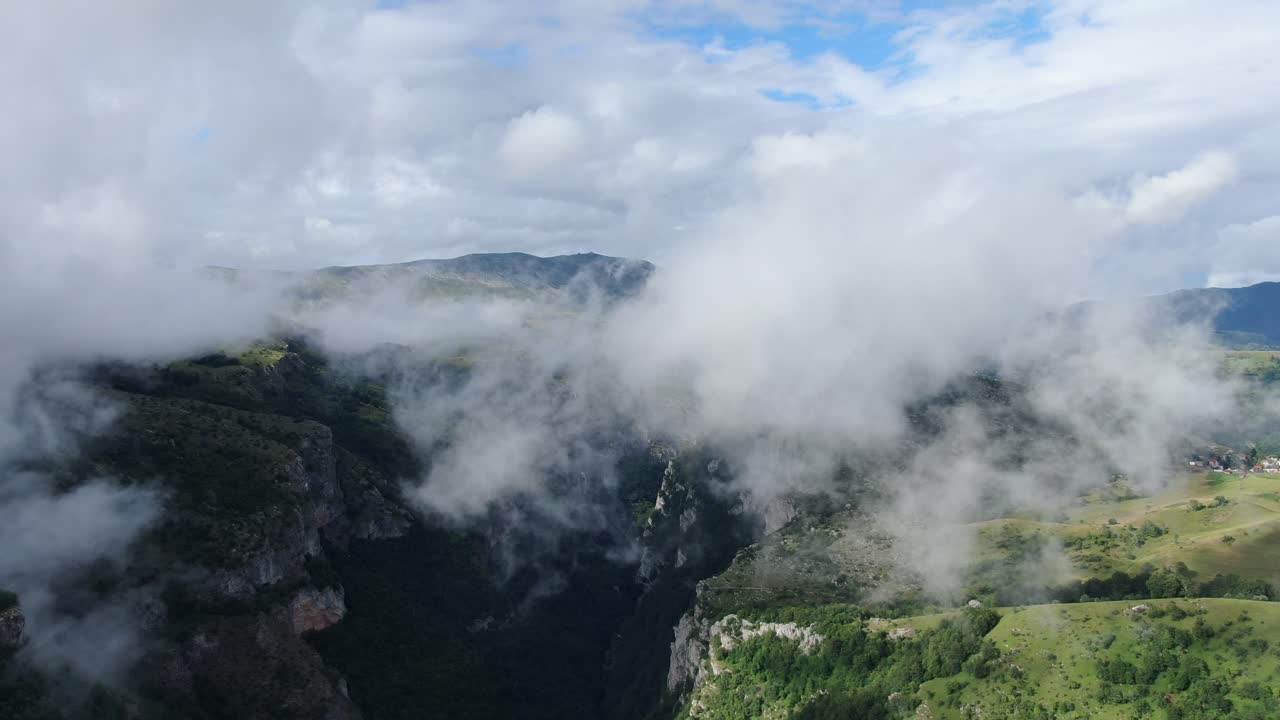 Dramatic aerial view of a mountain valley filled with low hanging clouds partially obscuring the lush green terrain A distant village adds to the scenic panorama