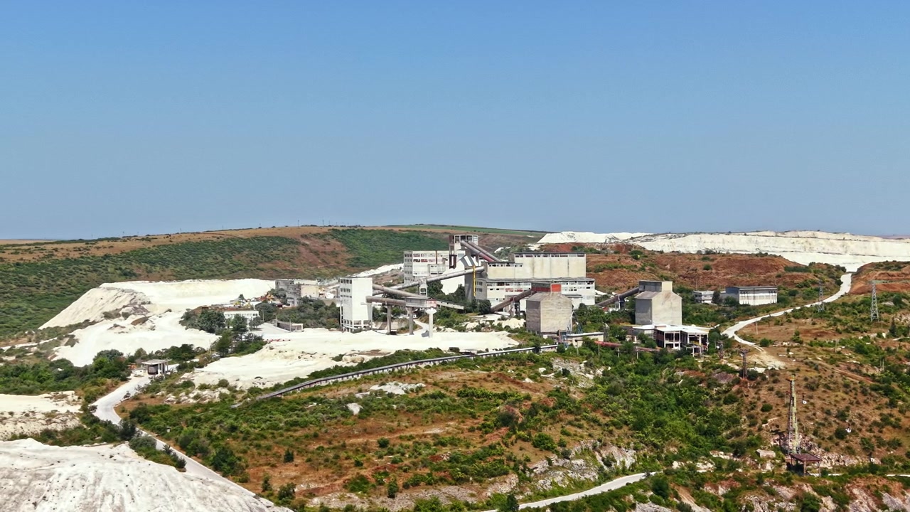 Sito di estrazione mineraria situato vicino a una collina con macchinari ed edifici sotto un cielo azzurro e limpido.