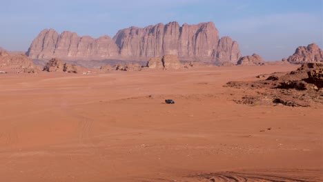 Solo-grey-4WD-truck-driving-across-vast-red-sand-desert-in-Wadi-Rum-with-rugged-sandstone-and-granite-mountains-in-the-distance-in-Jordan