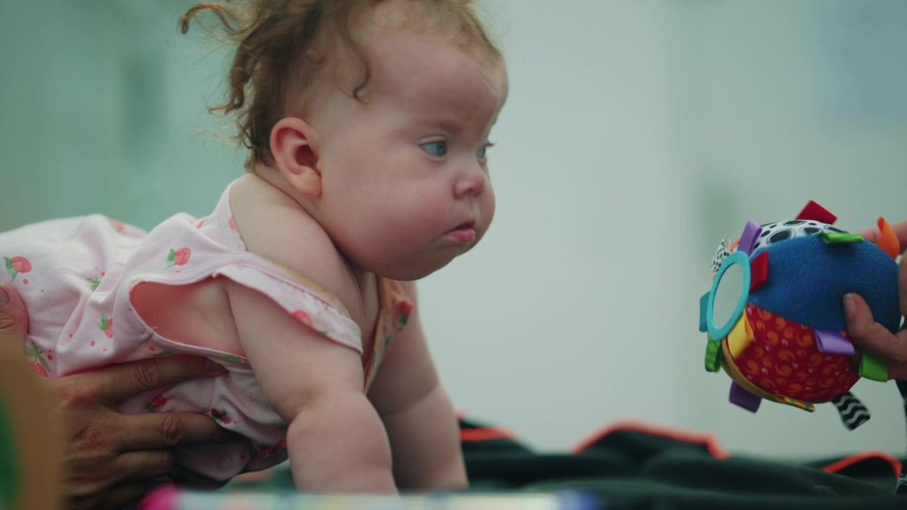 Baby girl on belly interacting with a colorful soft toy ball, developing motor skills during early childhood
