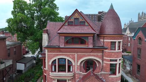 Elegant-brick-Victorian-home-with-intricate-architectural-details,-surrounded-by-lush-greenery-in-an-urban-setting