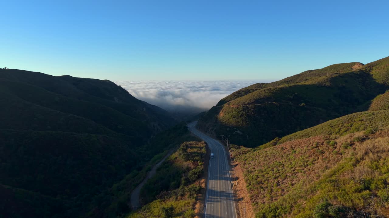 Dirigindo pelo cânion de Malibu, acima da neblina e das nuvens costeiras. Vista matinal de drone de carros dirigindo. Localização: Montanhas de Santa Monica, Califórnia. Vista do vale montanhoso e enevoado