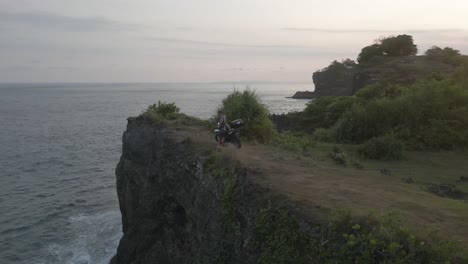 aerial orbits male motorcycle tourist atop tall ocean cliffs in bali