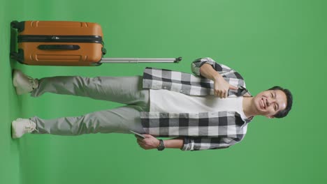 full body of asian male traveler with luggage and passport smiling and showing thumbs up gesture to the camera while standing in the green screen background studio