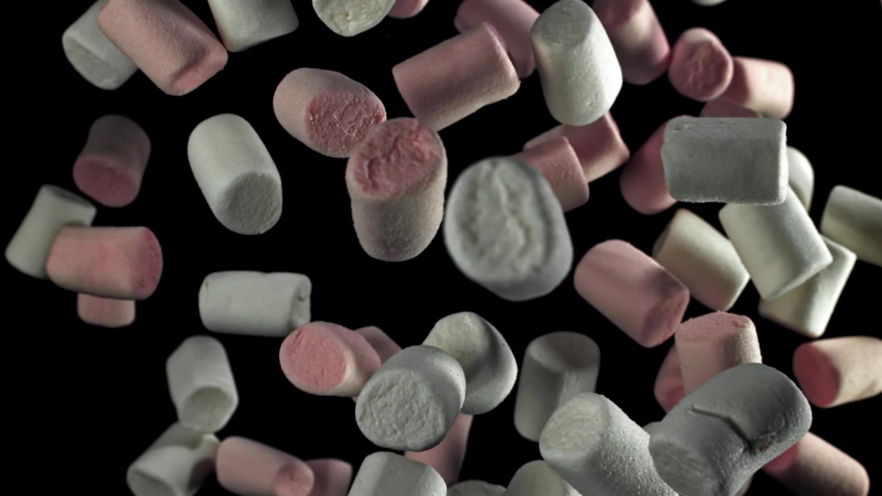 Marshmallow rosa e bianchi che cadono al rallentatore su sfondo nero.