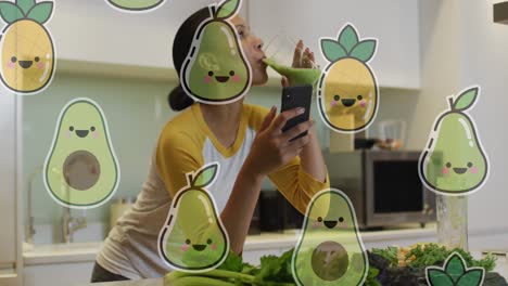 animation of smiling fruits over biracial woman having health drink and using smartphone at home