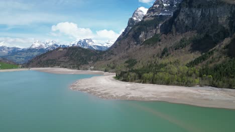 Aerial-forward-view-of-shoreline-of-an-alpine-lake-in-a-fantastic-mountain-landscape