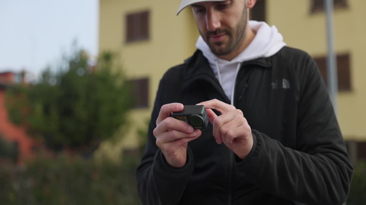 hombre con barba y gorra cambiando los ajustes en la pantalla táctil de la cámara dji osmo action 4 al aire libre
