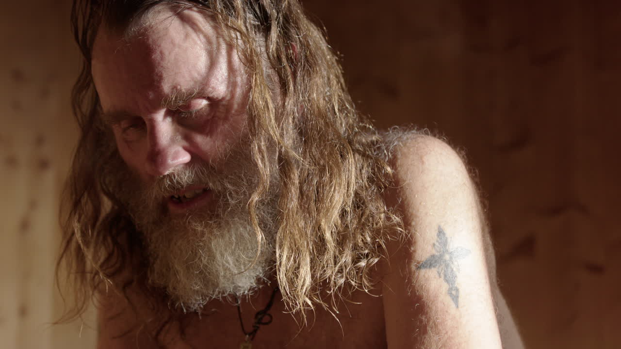 Viking Nordic man pours water on hot stones creating steam in wooden sauna