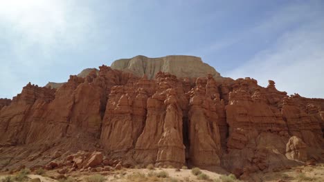 Tilt-up-shot-revealing-large-red-rock-formations-with-a-red-and-white-rock-butte-on-a-hike-inside-of-the-Utah-State-Park-Goblin-Valley-on-a-warm-sunny-summer-day