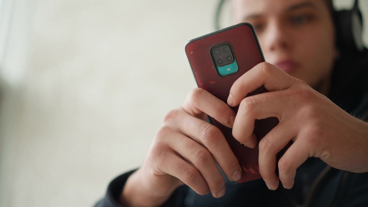 Close up of hands holding red smartphone with multiple camera lenses fingers interacting steadily. Soft lighting highlights texture and details of skin on hand and phone case. Indoor setting
