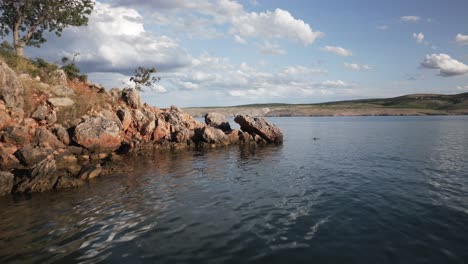 Ein-Mann-Schwimmt-Im-Meer-Nahe-Der-Küste-In-Goldon-Hour-Mit-Bergen-Im-Hintergrund