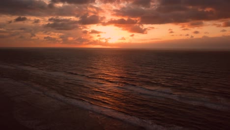 Absteigende-Drohnenaufnahme-Des-Orangefarbenen-Himmels-Und-Des-Ozeans-Bei-Sonnenaufgang,-Itanhaem,-Brasilien