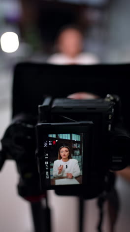 distancing from a display of a professional camera recording a brunette long-haired woman. blog creation. blurred backdrop. vertical video.