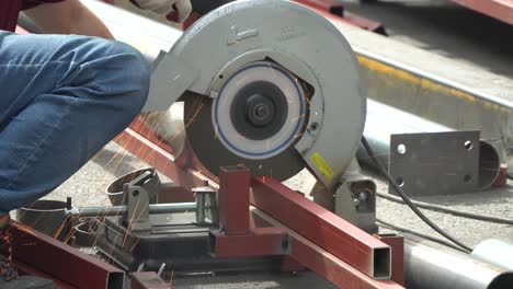 construction site, male worker cutting a metal tubular with cut-off machine - close up side view