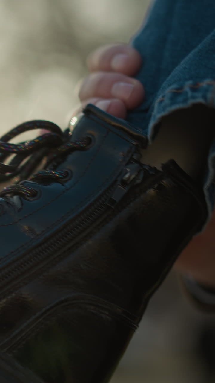 un primer plano de la pierna de un niño con pantalones vaqueros azules y una bota negra. el niño está siendo sostenido, con el fondo con un entorno al aire libre con árboles y luz solar