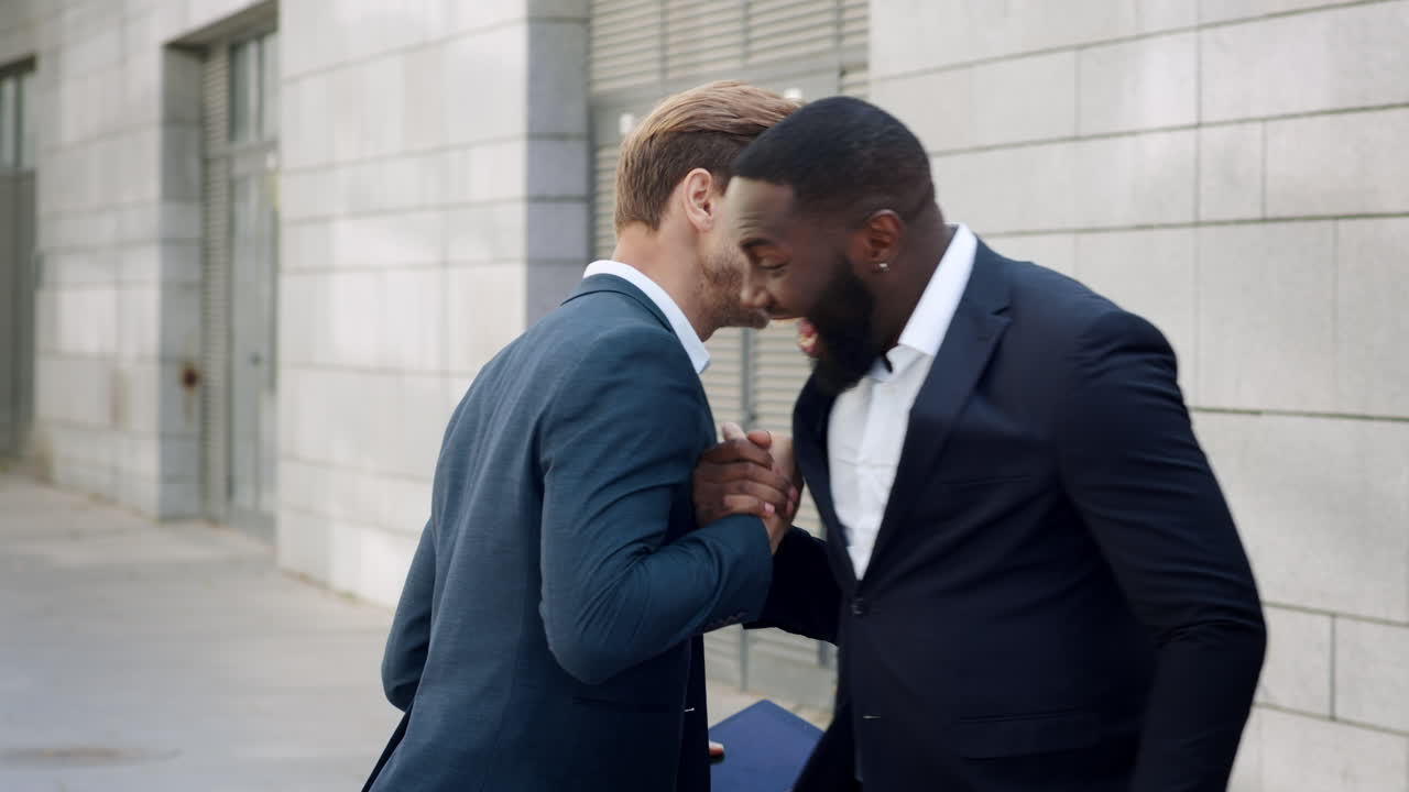 Businessmen receiving good news on tablet at street. Business partners hugging