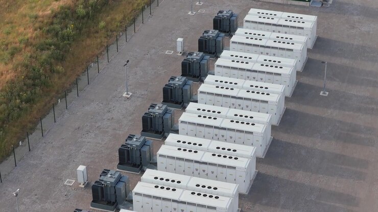 Aerial view of battery storage units in neat rows at a power station, managing renewable energy for the local grid on a clear day.