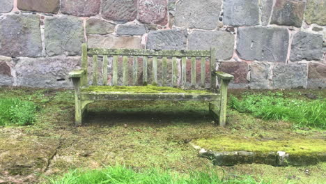 old mossy wooden bench against stone wall
