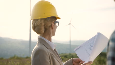 mujer caucásica ingeniera con casco viendo algunos planos y hablando con su compañero de trabajo en la estación eólica de energía renovable