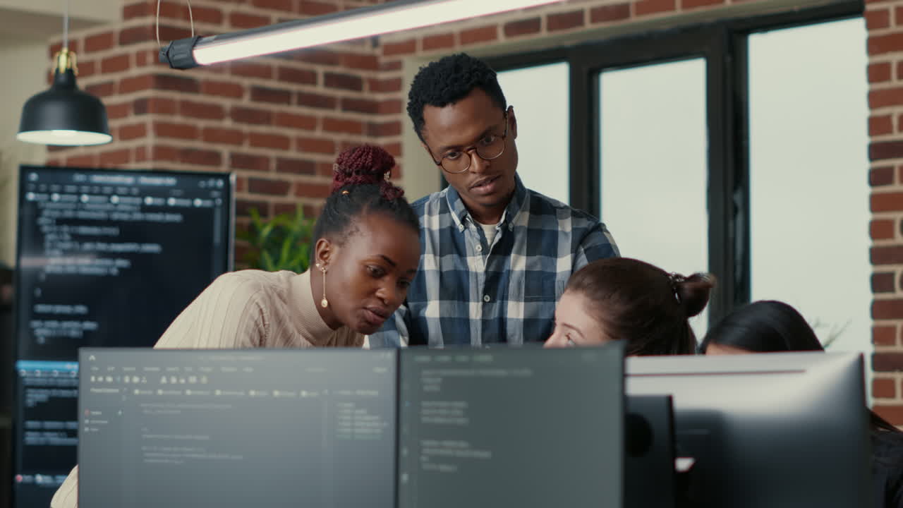 Developers brainstorming ideas looking at code on computer screens asking feedback from senior developer