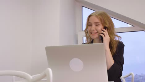 mujer de negocios sonriente hablando por teléfono móvil mientras trabaja en la computadora portátil en la oficina