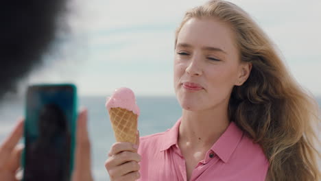 Schöne-Blonde-Frau-Mit-Afro,-Die-Am-Strand-Eis-Isst-Und-Für-Einen-Freund-Posiert,-Der-Mit-Dem-Smartphone-Ein-Foto-Macht.-Freundinnen-Teilen-Lustigen-Sommertag-In-Den-Sozialen-Medien-4K