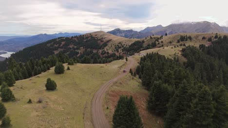 Car-drives-along-winding-dry-dirt-road-along-ridgeline-forest-with-grandiose-mountains-of-Agrafa-Greece