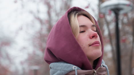 close-up of woman wearing a hooded winter jacket, smiling warmly while strolling through a serene, snow-covered environment, blurred background with bare trees and red berries