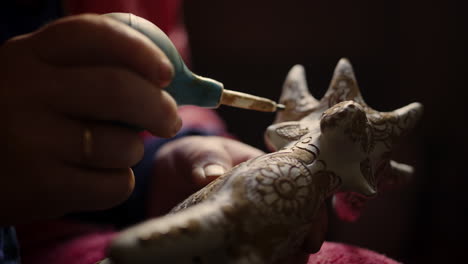 mano de mujer en primer plano decorando un producto en cerámica. ceramista pintando un ciervo de juguete