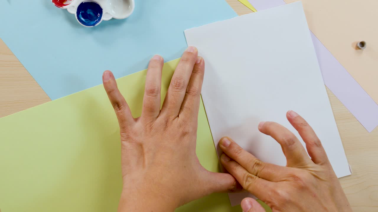 Hands fold paper over paint drops to create a colorful symmetrical blot art piece