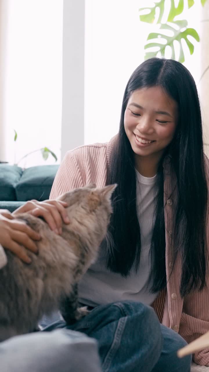 Gelukkige jonge Aziatische vrouw aait lachend een kat thuis